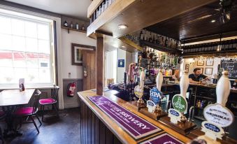 a bar with a purple and white striped tablecloth , multiple beer taps , and a variety of bottles on display at The Bell Inn