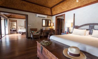 a spacious bedroom with a king - sized bed , a wooden dresser , and a potted plant on the floor at Small Luxury Hotels of the World - Pacific Resort Aitutaki
