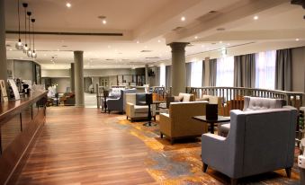 a spacious room with wooden floors , large windows , and various seating arrangements , including couches , chairs , and tables at DoubleTree by Hilton Swindon