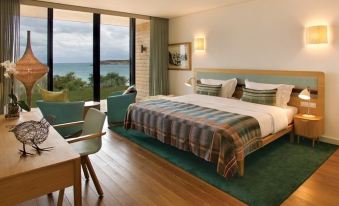 a hotel room with a king - sized bed , a dining table , and a view of the ocean at Martinhal Sagres Beach Family Resort Hotel
