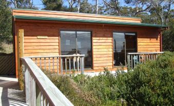 a wooden cabin with a green roof , surrounded by trees and grass , and located near a body of water at Bruny Island Escapes and Hotel Bruny