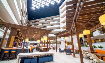 a large , modern hotel lobby with a high ceiling and wooden furniture , including couches , chairs , and tables at Embassy Suites by Hilton Kansas City Overland Park