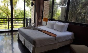 a large bed with white sheets and a wooden headboard is situated in front of a window at Suwan Golf & Country Club