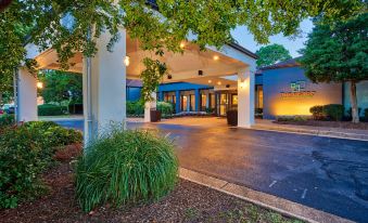 an entrance to a building with trees and bushes surrounding it , creating a serene and inviting atmosphere at Courtyard Hampton Coliseum Central