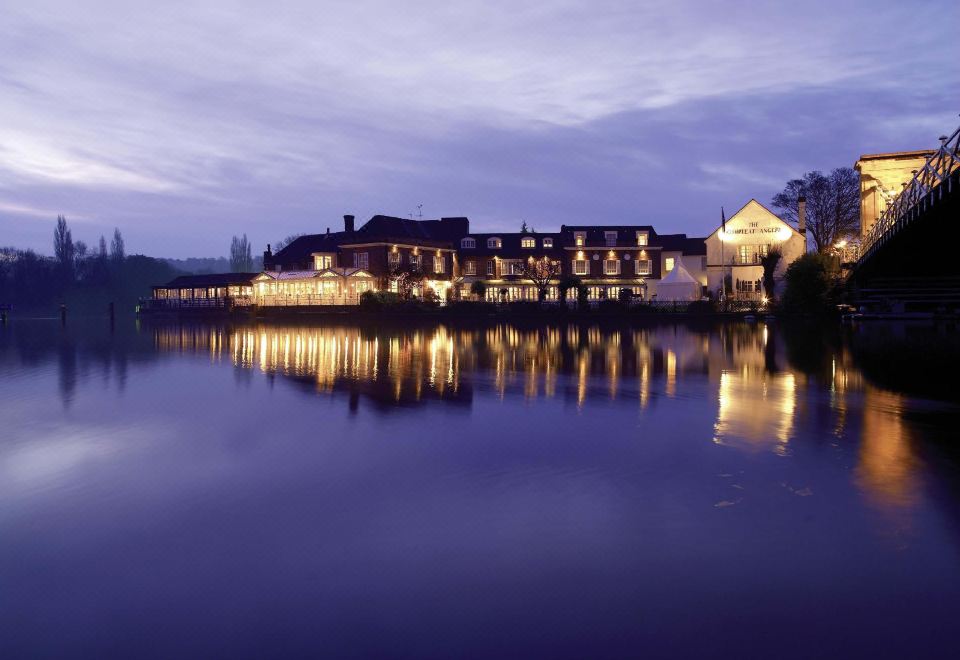 a beautiful nighttime scene of a large building near a lake , illuminated by lights and surrounded by trees at Macdonald Compleat Angler