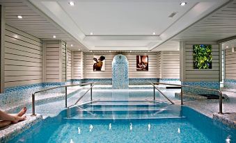 an indoor swimming pool with a waterfall feature , surrounded by a modern building with white walls and black - and - white checkered flooring at Hotel le Morgane