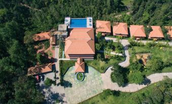 an aerial view of a large building surrounded by trees , with a pool in the foreground at Coorg Cliffs Resort