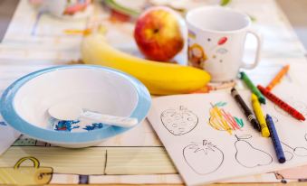 a table with a blue bowl , a mug , and a coloring page of fruit on it at NH Geneva City