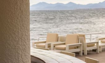 a row of white chairs on a balcony overlooking a body of water with mountains in the background at Cap d'Antibes Beach Hotel