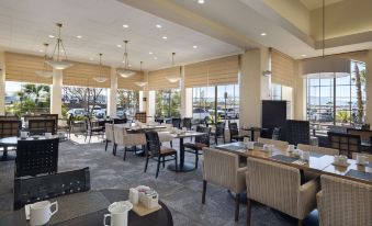 a modern , well - lit restaurant with large windows offering views of the city , featuring several dining tables and chairs at Hilton Garden Inn Las Vegas Strip South