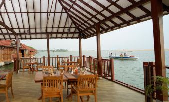 a wooden deck with chairs and tables , overlooking a body of water where people are enjoying the view at Poovar Island Resort