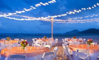 a beachside wedding reception with multiple tables set up for guests , surrounded by palm trees and a beautiful sunset at St. Kitts Marriott Resort & the Royal Beach Casino