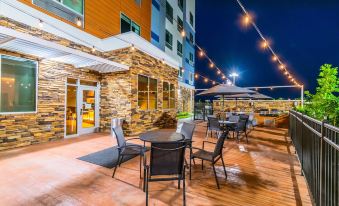an outdoor dining area with several tables and chairs , surrounded by a wooden deck and string lights at Fairfield Inn & Suites Houston League City