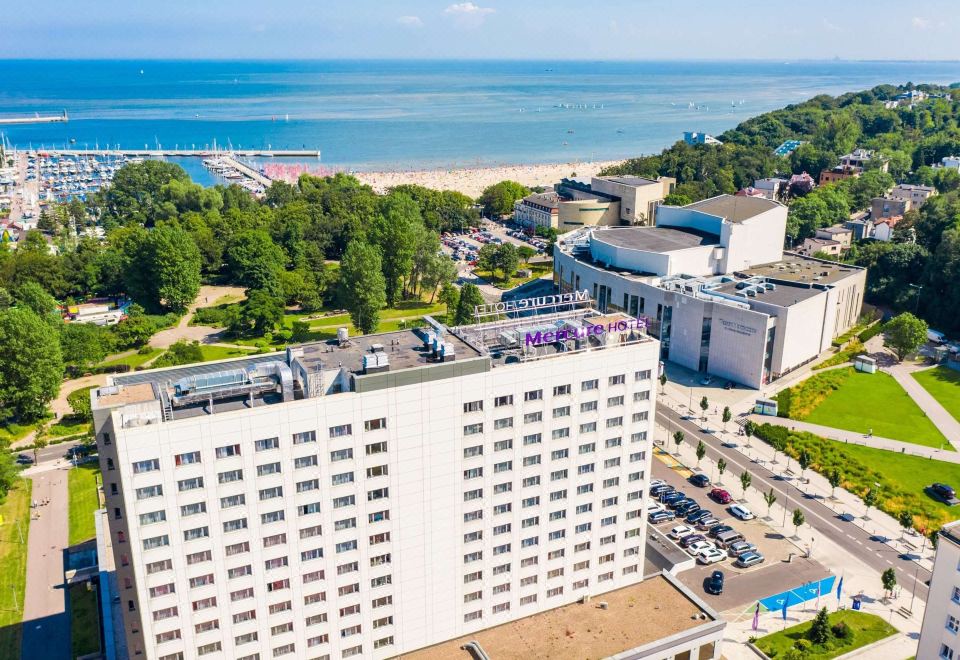 aerial view of a large white building near the ocean , surrounded by trees and cars parked on the street at Hotel Mercure Gdynia Centrum