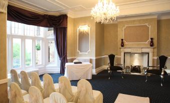 a room with a chandelier , chairs , and tables set up for an event , including a piano in the corner at Burnley West Higher Trapp Hotel