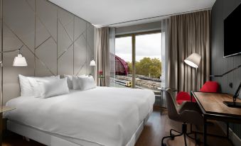 a hotel room with a large bed , a desk , and a window overlooking the city at NH Collection Antwerp Centre