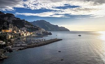 a picturesque view of a coastal town with mountains in the background , and boats on the water at Hotel Miramalfi