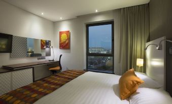 a hotel room with a king - sized bed , a desk , and a large window overlooking the city at Hotel Verde Cape Town Airport