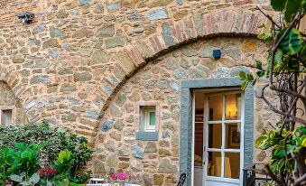 a stone house with an arched doorway and a table set for two outside , surrounded by greenery at Monastero di Cortona Hotel & Spa
