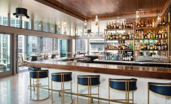 a modern bar with a wooden ceiling , black and white striped stools , and a variety of bottles on the shelves at The Charter Hotel Seattle, Curio Collection by Hilton