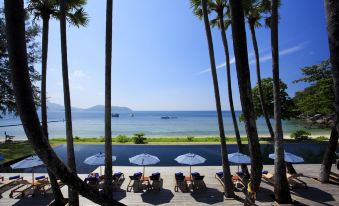 a beautiful view of the ocean from a deck , with several lounge chairs and umbrellas providing shade at The Naka Phuket