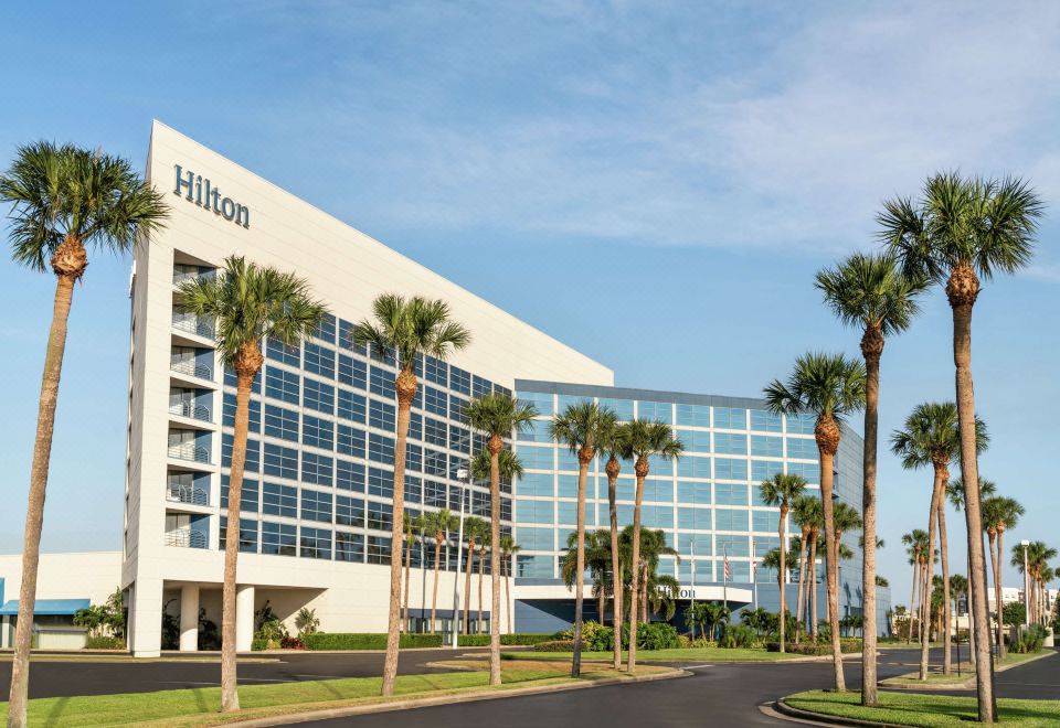 a large white hilton hotel surrounded by palm trees , with a blue sky in the background at Hilton Melbourne, FL