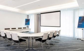 a conference room with a long table , chairs , and a projector screen on the wall at Novotel Lugano Paradiso