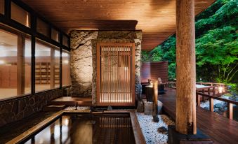 a japanese - style bathroom with a stone wall , wooden accents , and a large window , lit by candles and surrounded by stone flooring at Noboribetsu Grand Hotel