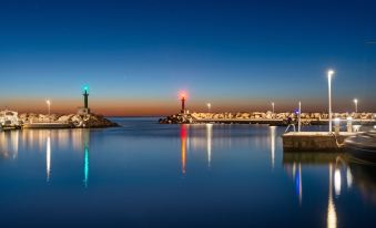 a serene nighttime view of a harbor with lighthouses and reflections in the water , illuminated by colorful lights at Cala Bona