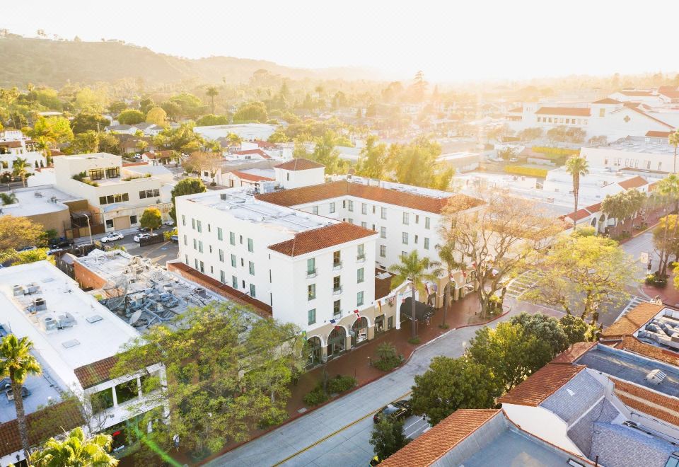 aerial view of a white building surrounded by trees and a body of water , with the sun setting in the background at Hotel Santa Barbara