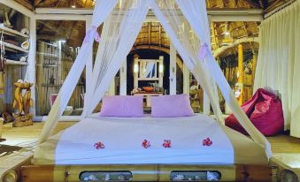 a bed with white sheets and a pink floral design is in a room with a wooden floor at Coconut Garden Beach Resort