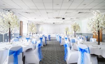a large banquet hall with white tables and chairs , blue ribbons on the backs , and a backdrop of white trees at Holiday Inn Leeds - Wakefield M1, Jct.40