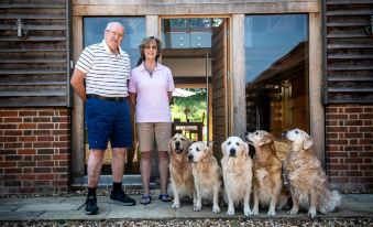 a man and a woman are standing in front of a wooden house , posing with a group of dogs at South Park Farm Barn