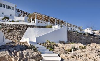 a white building with a stone wall and steps leading up to it , surrounded by rocks and plants at Notos Therme and Spa