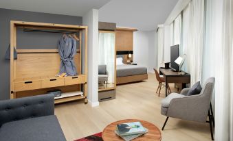 a modern bedroom with a bed , desk , and chair is connected to a living area with a couch and bookshelf at Canopy by Hilton Ithaca Downtown