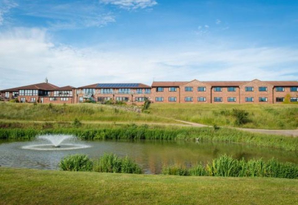a large building with a fountain in front of it , surrounded by grass and a pond at Greetham Valley