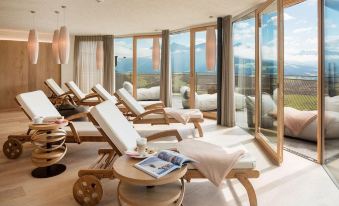 a luxurious spa setting with wooden lounge chairs and large windows , providing a panoramic view of the mountains at Alpin Panorama Hotel Hubertus