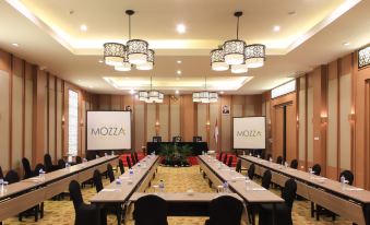 "a conference room with long tables , chairs , and two large screens displaying the word "" moza "" and "" mwc "" in the background" at Swiss-Belinn Timika