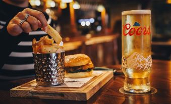 a person is eating french fries and drinking a beer at a bar , surrounded by various food items at The Knaresborough Inn - the Inn Collection Group
