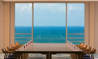 a long wooden table is set with wine glasses and chairs in front of a large window overlooking the ocean at Kaike Tsuruya