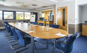 a large conference room with a long wooden table surrounded by chairs and several bottles of water at Holiday Inn Express Northampton - South