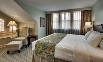 a large bed with a colorful blanket is in the center of a room with two chairs and windows at The Inn at Wise