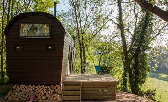 a small wooden house is nestled in a forested area with a deck and chair nearby at Extraordinary Huts