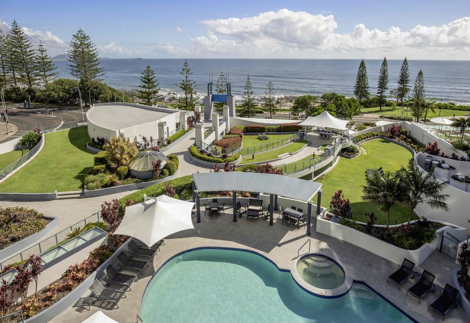 a resort with a pool surrounded by lounge chairs and umbrellas , overlooking the ocean at Mantra Mooloolaba Beach