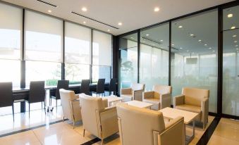 a modern office lounge area with multiple chairs and tables , surrounded by large windows that offer a view of the outdoors at Dormy Inn Mishima