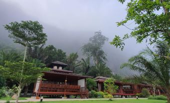 a tropical resort with wooden buildings surrounded by lush greenery and misty mountains , under a cloudy sky at Phuphayot Resort