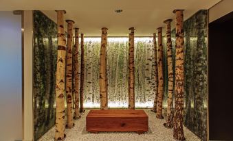 a room with a wooden table and several tall birch trees in the center , surrounded by green plants at Steigenberger Airport Hotel Berlin