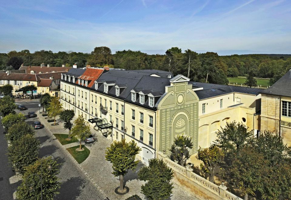 an aerial view of a large building with a clock tower , surrounded by trees and cars at Auberge du Jeu de Paume