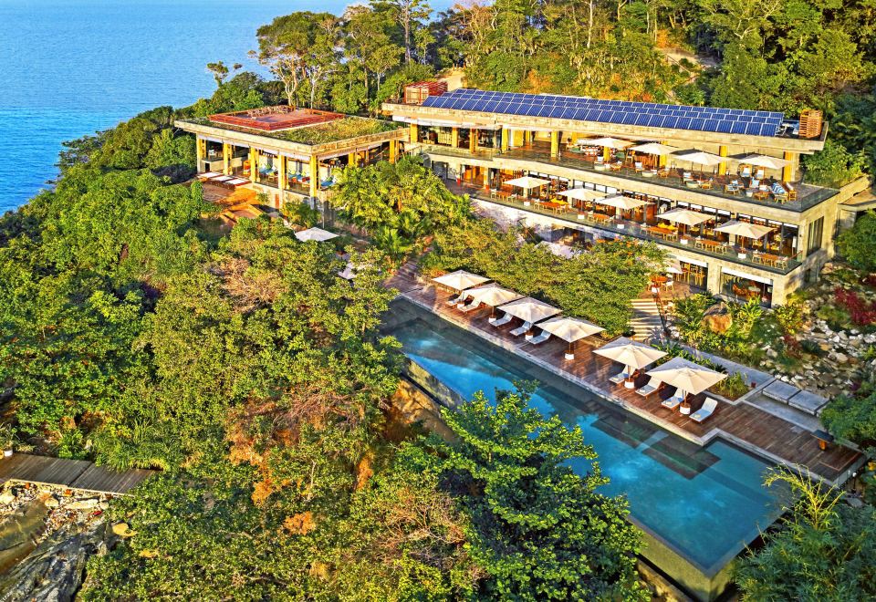 a large building with a swimming pool is situated on a hillside overlooking the ocean at Six Senses Krabey Island