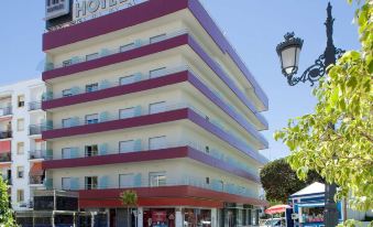 a red and white striped hotel building with a sign on top , situated in a city street at NH San Pedro